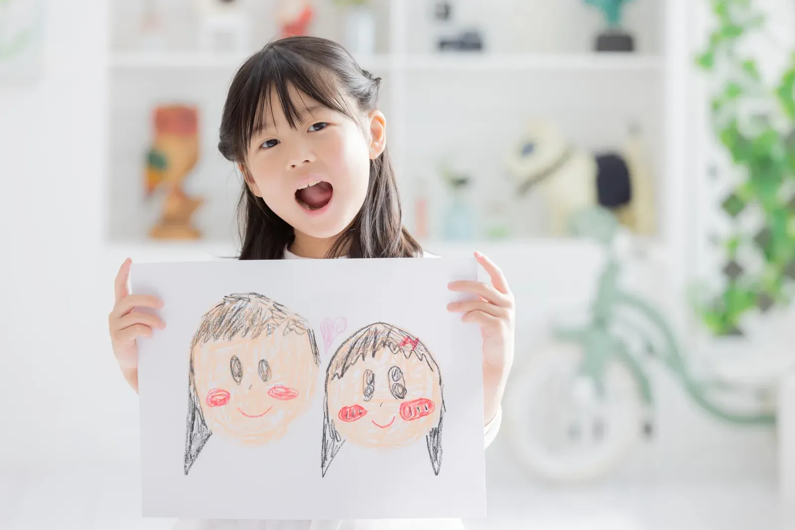 子どもの絵を見せ、親がしゃがんで目線を合わせて聞いている温かいワンシーン