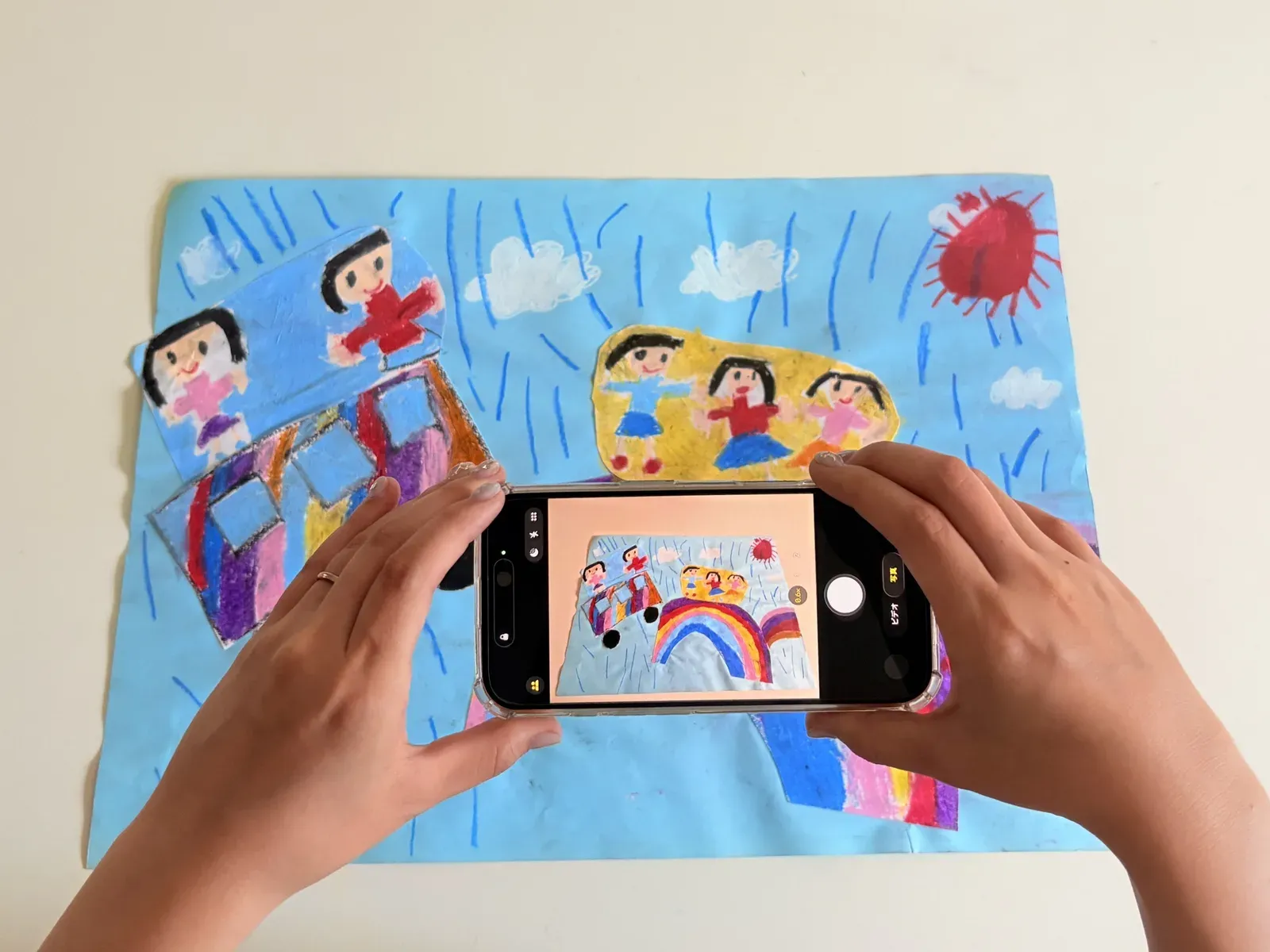 子どもの絵をスマホで撮影している手元のイメージ