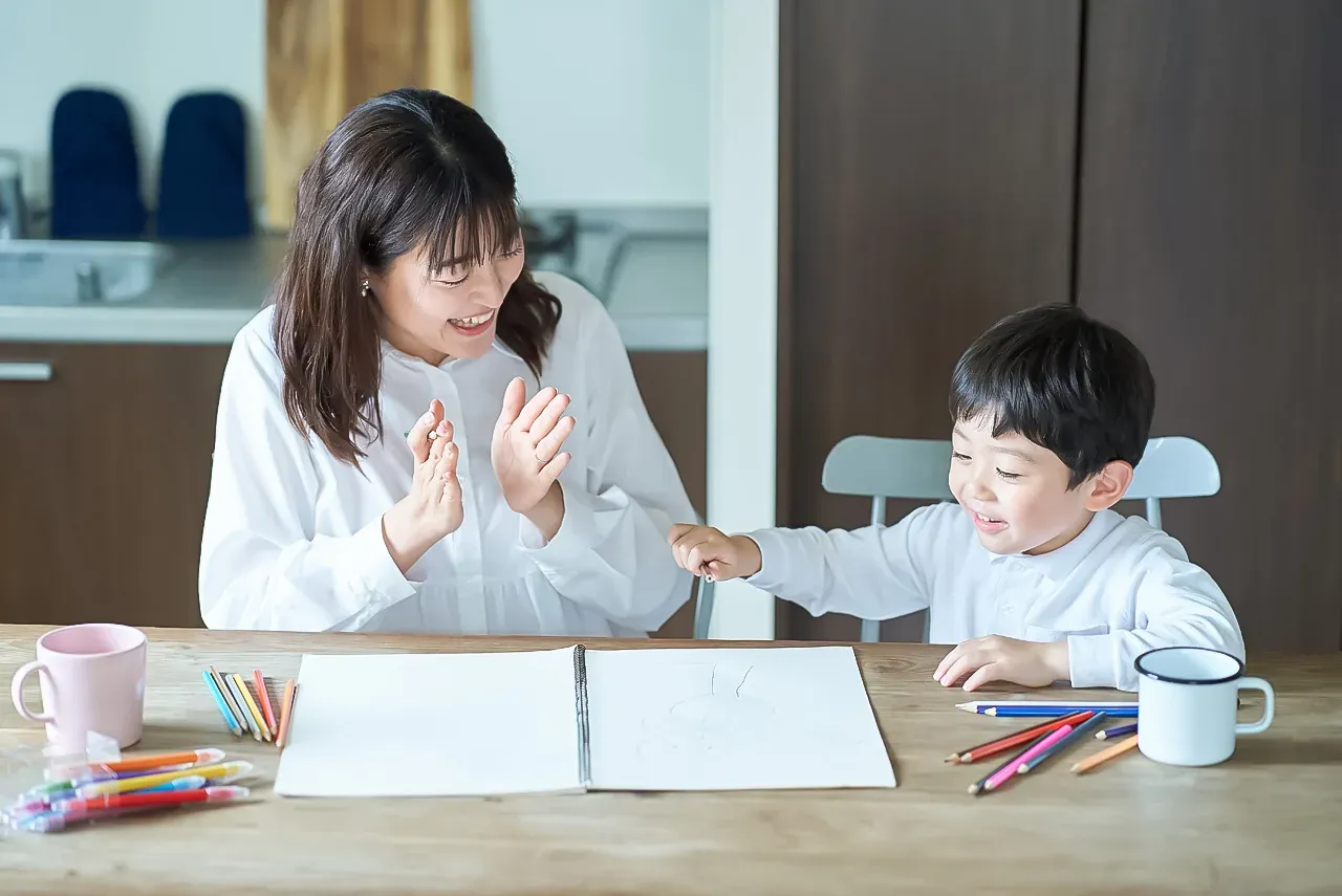 子どもが描いた絵を見せ、親が拍手と笑顔で受け止めている様子