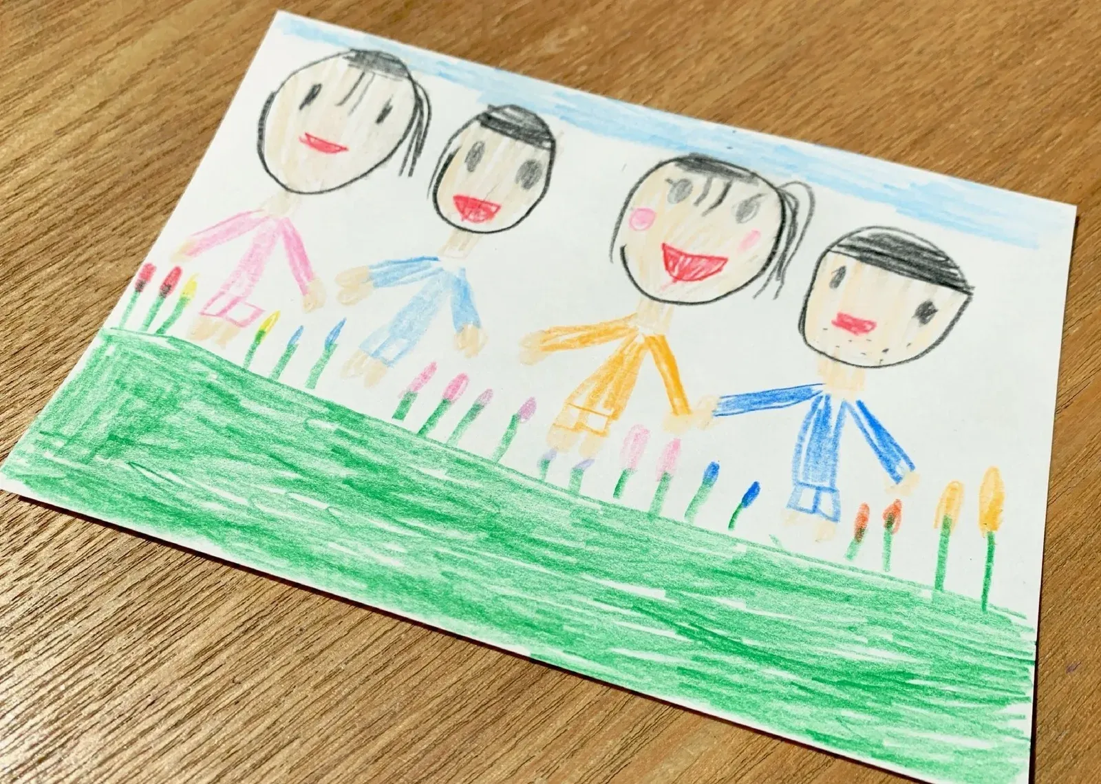 子どもが色えんぴつで描いた、並んで立つ家族4人の絵